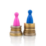 Pink and blue figures on different coin stacks. Concept for gender pay gap.